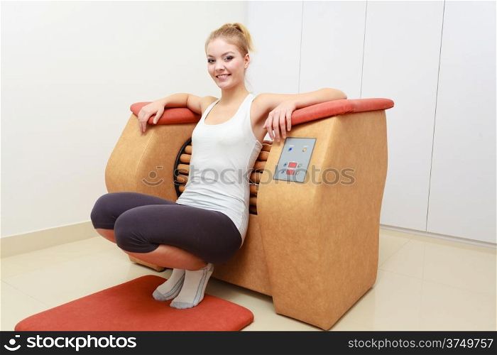 Smiling blond girl in sportwear using on modern relax massage equipment. Young woman doing relaxation exercise in healthy spa salon.