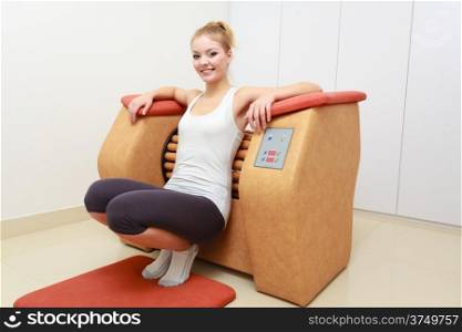 Smiling blond girl in sportwear using on modern relax massage equipment. Young woman doing relaxation exercise in healthy spa salon.