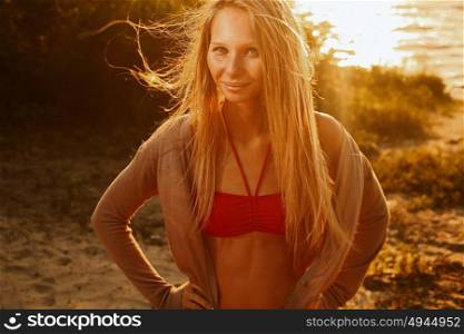 Smiling blond haired woman posing on sunset beach in front of water full of warm sunshine. Smiling blond haired woman posing on sunset beach in front of water retro color full of warm sunshine