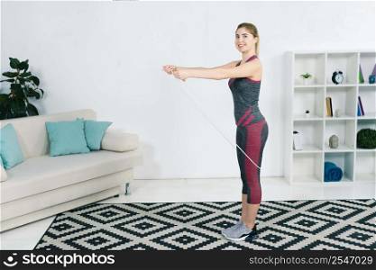 smiling blonde young woman exercising with skipping rope home living room