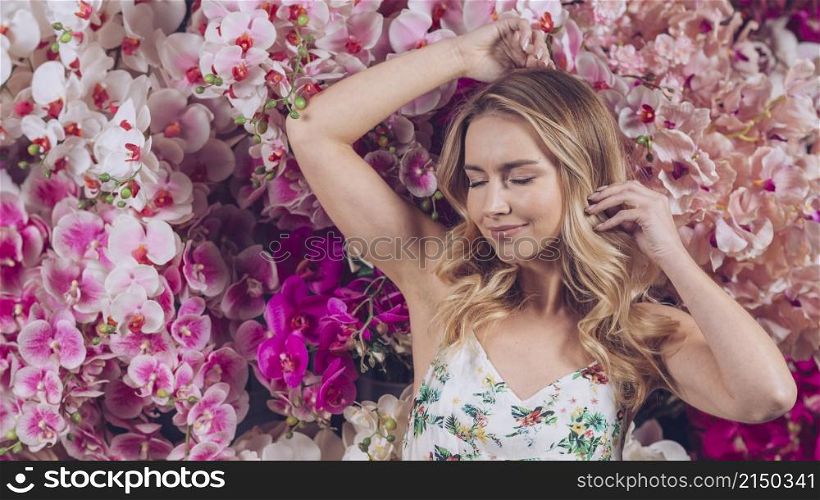 smiling blonde young woman with eye closed standing against colorful orchids