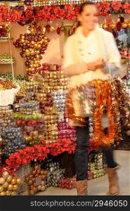 Smiling blurry woman buying shiny Christmas ornaments in shop