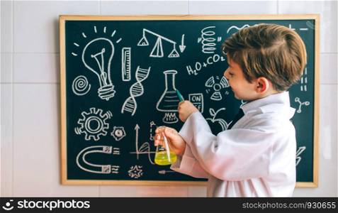 Smiling boy dressed as chemist with flask pointing at a blackboard with drawings