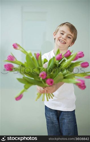 Smiling boy holding out tulip flowers against gray background