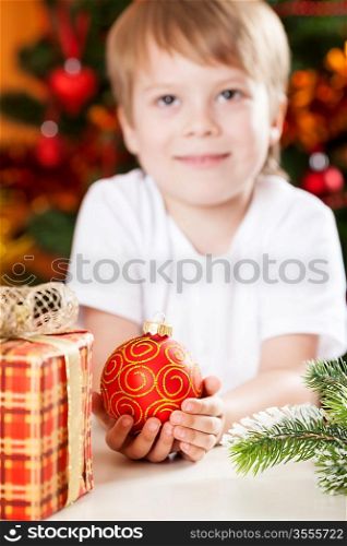 Smiling boy holding red ball against Christmas lights