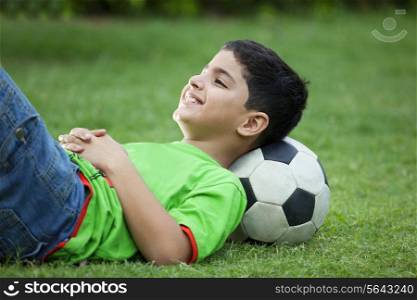 Smiling boy lying on grass with soccer ball
