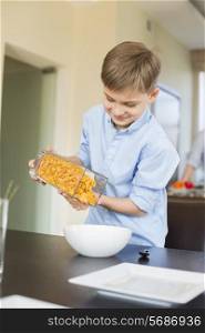 Smiling boy pouring corn flakes in bowl at home