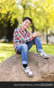Smiling boy wearing casual clothes while sitting on rock at city park