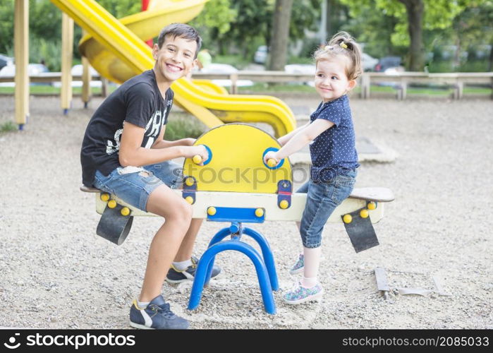 smiling brother sister playing seesaw playground