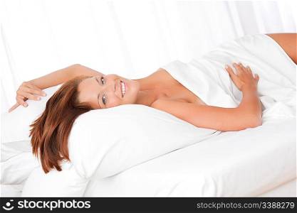 Smiling brown hair woman lying in white bed, shallow depth-of-field