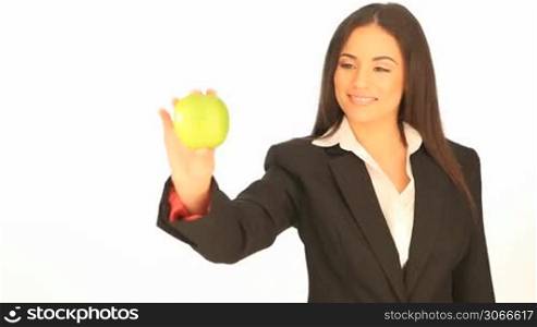 Smiling brunette businesswoman holding up a fresh green apple on display in her hand against a white background