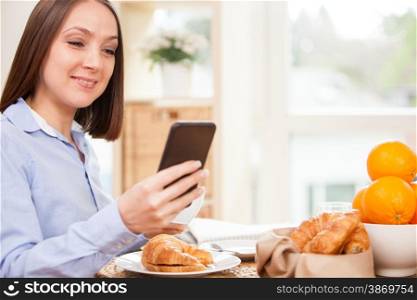 Smiling brunette businesswoman is having breakfast while checking her emails at home