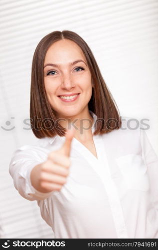 Smiling brunette businesswoman is making positive thumb gesture over white background