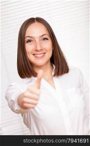 Smiling brunette businesswoman is making positive thumb gesture over white background