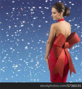 smiling brunette female posing with sexy red christmas dress and big glitter bow turned on her naked back, wearing golden jewellery