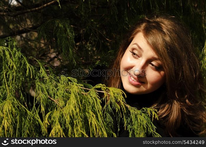 Smiling brunette girl behind the tree under the spring sunlight.Shallow deep of field