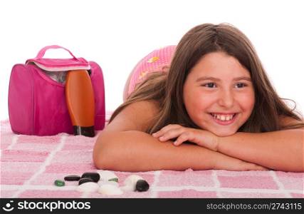 smiling brunette teenage girl in swimsuit lying at the beach (studio setting with bag, pink towel, sun lotion and little stones) isolated on white background