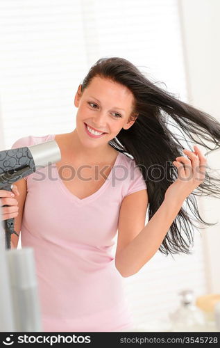 Smiling brunette woman blow-drying long hair in bathroom