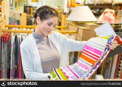 smiling brunette woman choosing fabric in textile shop