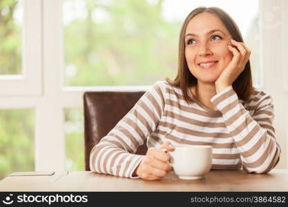 Smiling brunette woman having a cup of coffee while sitting and thinking at home