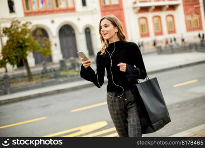 Smiling brunette woman using mobile while standing on street and  waiting for a bus or taxi