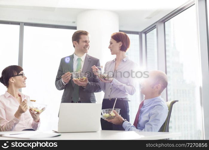 Smiling business colleagues eating lunch in boardroom during meeting at office