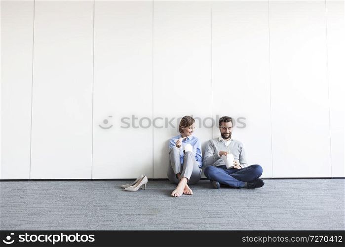 Smiling business colleagues having food while sitting on floor at office