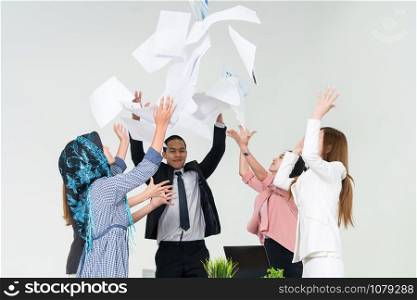 Smiling business people having fun by throwing papers in the air celebrating business success in the modern office. Happy workplace and casual career company concept.