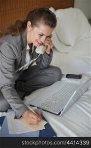 Smiling business woman having working phone calls on bed in hotel room