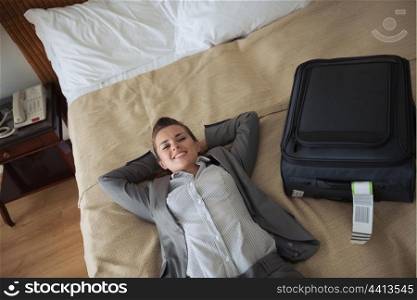 Smiling business woman laying on bed in hotel room