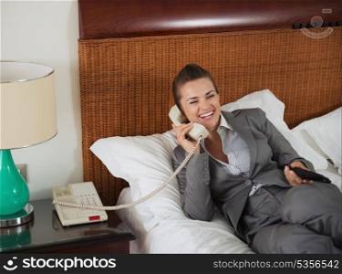 Smiling business woman laying on bed talking phone in hotel room
