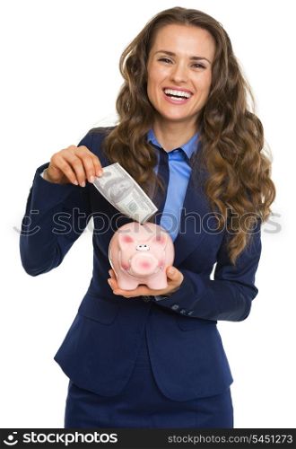 Smiling business woman putting 100 dollars banknote into piggy bank