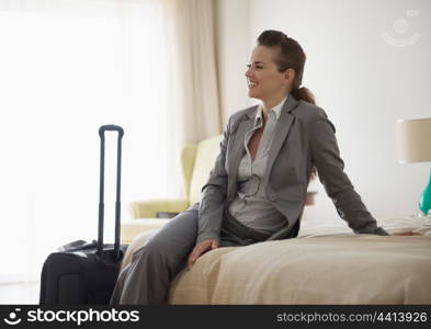 Smiling business woman sitting on bed in hotel room