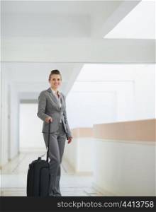 Smiling business woman with bag on wheels in business trip