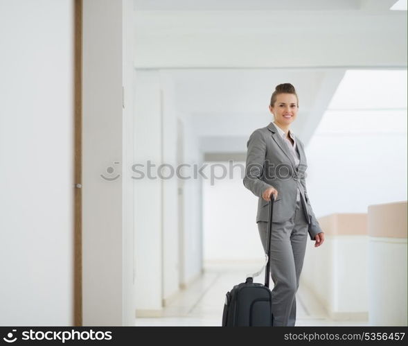 Smiling business woman with bag on wheels in business trip