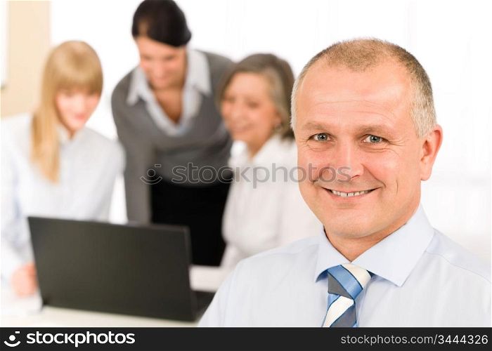 Smiling businessman during team meeting with colleagues looking at laptop