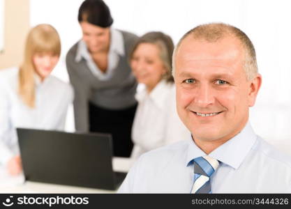 Smiling businessman during team meeting with colleagues looking at laptop