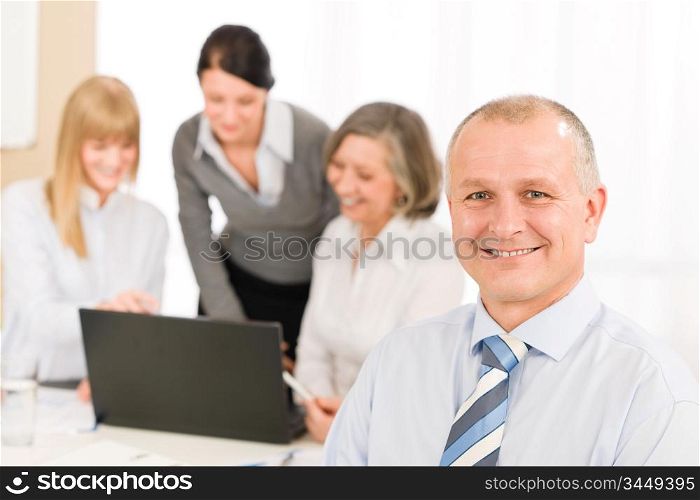 Smiling businessman during team meeting with colleagues looking at laptop