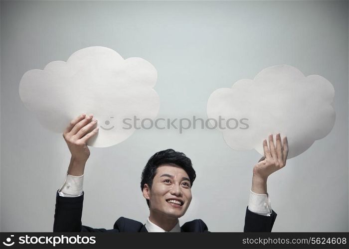 Smiling businessman holding two paper clouds, studio shot