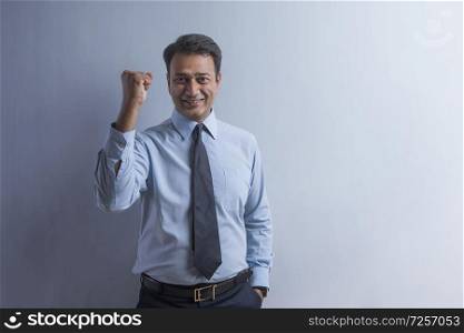 Smiling businessman in formal clothes showing raised fist with one hand symbolising strength and confidence