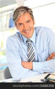 Smiling businessman in office with arms crossed