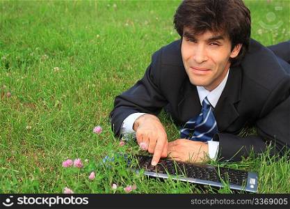 smiling businessman lies on grass with laptop