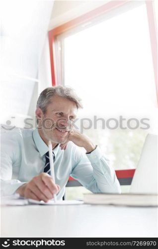 Smiling businessman looking at laptop by window in office
