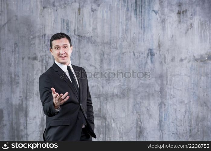smiling businessman pointing camera while standing against grey wall