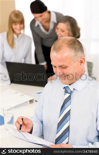 Smiling businessman read report during meeting with team colleagues