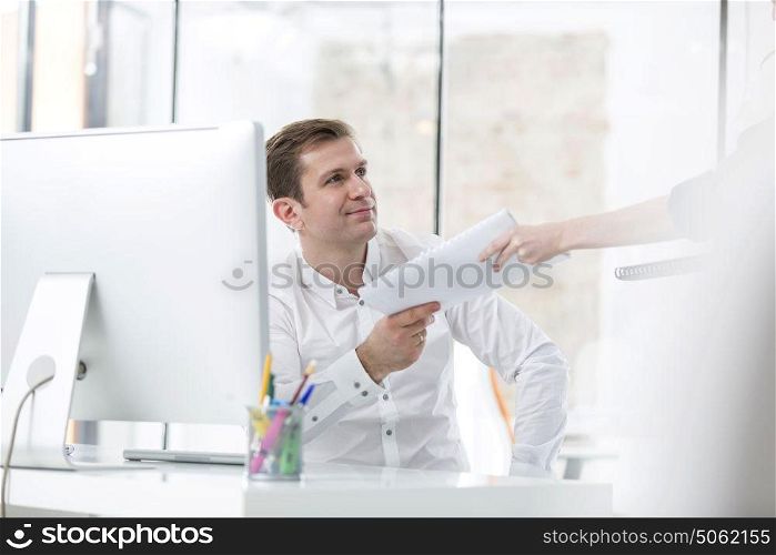 Smiling businessman receiving book from colleague in office