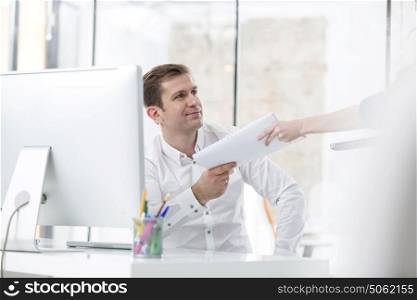 Smiling businessman receiving book from colleague in office