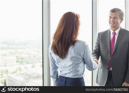 Smiling businessman shaking hands with businesswoman in office