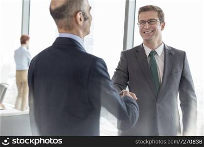 Smiling businessman shaking hands with colleague in boardroom during meeting at office