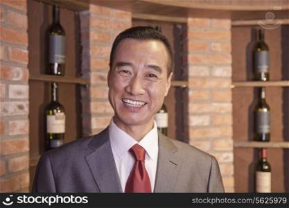 Smiling Businessman Standing by Wine Bottles
